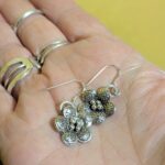 E100 Ella Earrings. Flower shaped and embossed with oxidised stamping, these silver earrings are small dangle drops. Handcrafted from fine silver and Fair Trade.
