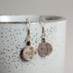 E048 Tia Earrings. Disc shaped silver dangle drops. With oxidised stamped flowers. Fine silver. Fair Trade. Recycled silver