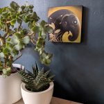 'Horizons' is a mounted print of a brown elephant against a golden background with botanical detailing