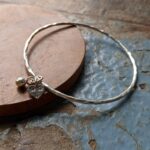 B016 Belle Bangle. Complete and continuous round bangle with a hammered and textured finish. Completed with a small round charm and an additional hallmarked heart charm.