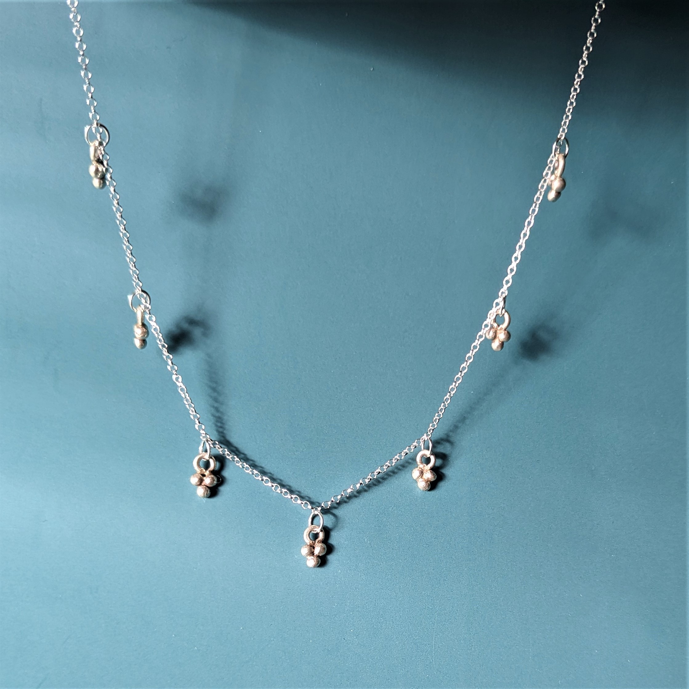 N112 Celeste Necklace. A sterling silver chain holds seven tiny ball cluster charms which are interspaced along the chain. Fair Trade and ethically handmade.