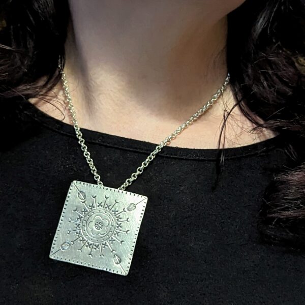 HL746 Ostara Necklace. Fair Trade, handmade from recycled silver this pendant is completed with a handcrafted hill tribe silver chain with a t-bar clasp. The square pendant has oxidised stamped detailing of flowers, leaves and geometric patterns.