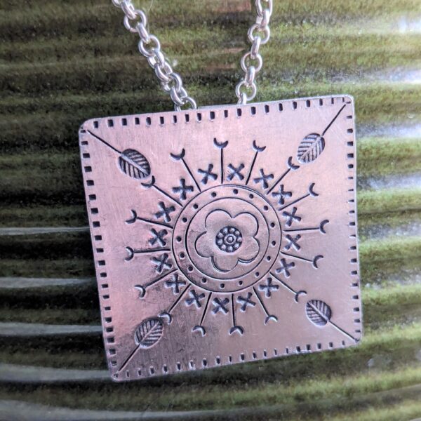 HL746 Ostara Necklace. Fair Trade, handmade from recycled silver this pendant is completed with a handcrafted hill tribe silver chain with a t-bar clasp. The square pendant has oxidised stamped detailing of flowers, leaves and geometric patterns.