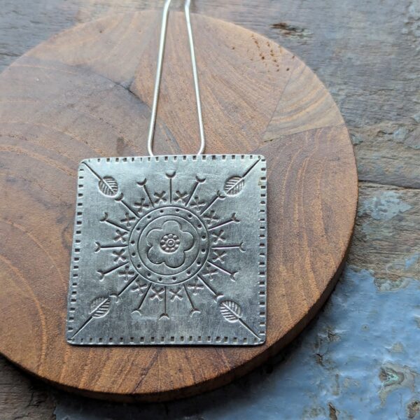 HL747 Ostara Necklace. Fair Trade, handmade from recycled silver this pendant can be strung on either a tough nylon cord or a snake chain. The square pendant has oxidised stamped detailing of flowers, leaves and geometric patterns.