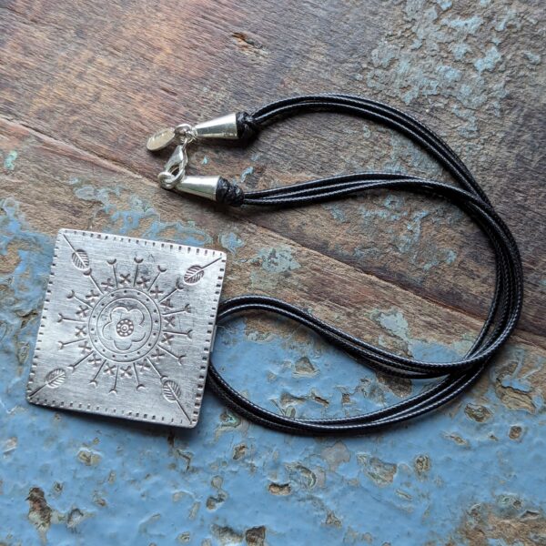 HL747 Ostara Necklace. Fair Trade, handmade from recycled silver this pendant can be strung on either a tough nylon cord or a snake chain. The square pendant has oxidised stamped detailing of flowers, leaves and geometric patterns.