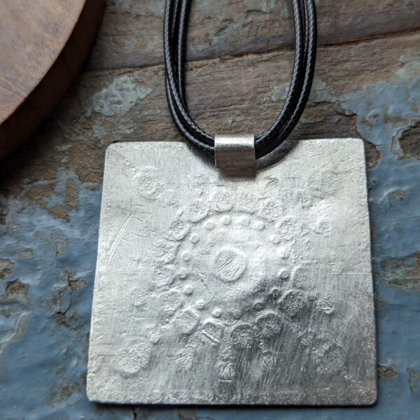 HL747 Ostara Necklace. Fair Trade, handmade from recycled silver this pendant can be strung on either a tough nylon cord or a snake chain. The square pendant has oxidised stamped detailing of flowers, leaves and geometric patterns.